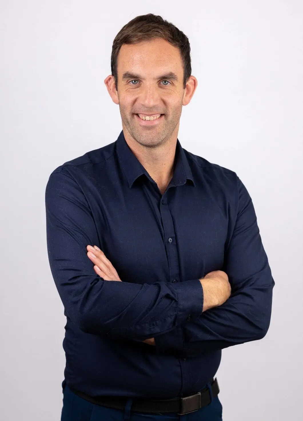 Will Jenkins, in a navy shirt, stands with arms crossed against a light background, looking at the camera.