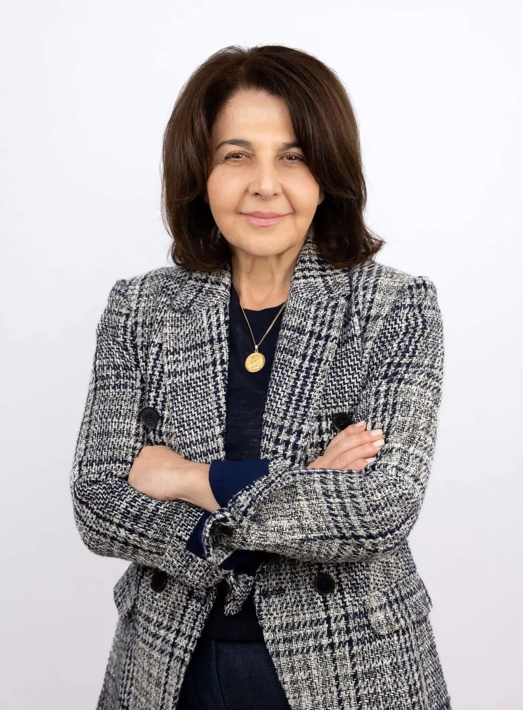 Mia Doumias of Family Health Clinics stands confidently in a plaid blazer and navy top, arms crossed, on white.
