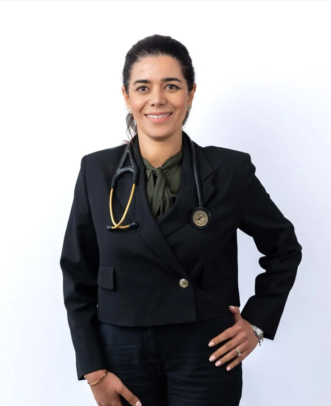 Dr Neda Beikaee, Family Health Clinics GP, smiles confidently in a black blazer with stethoscope on white background.