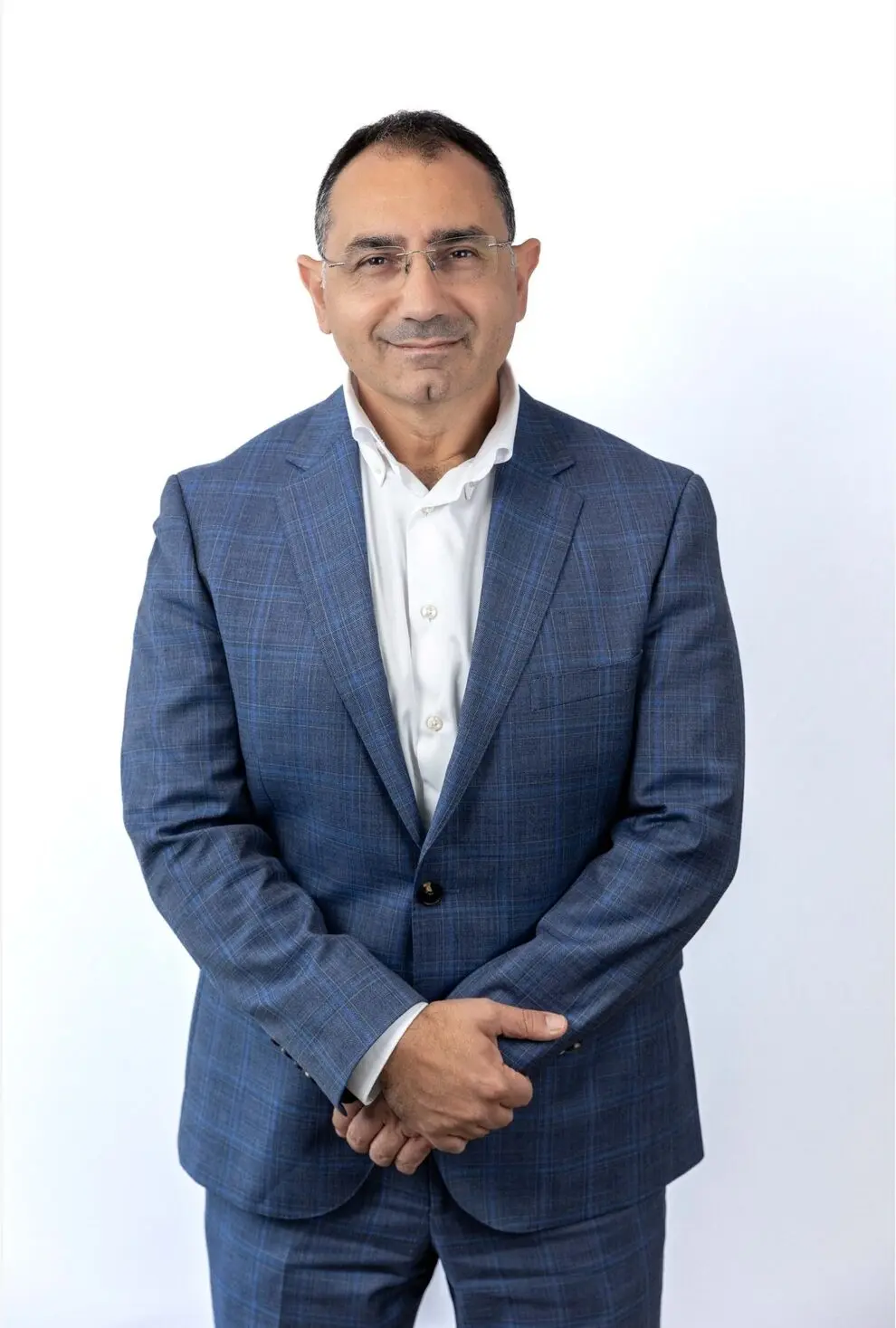 Dr Nadim Taoum, Family Health Clinics GP, in blue checked suit and white shirt, stands with hands clasped.
