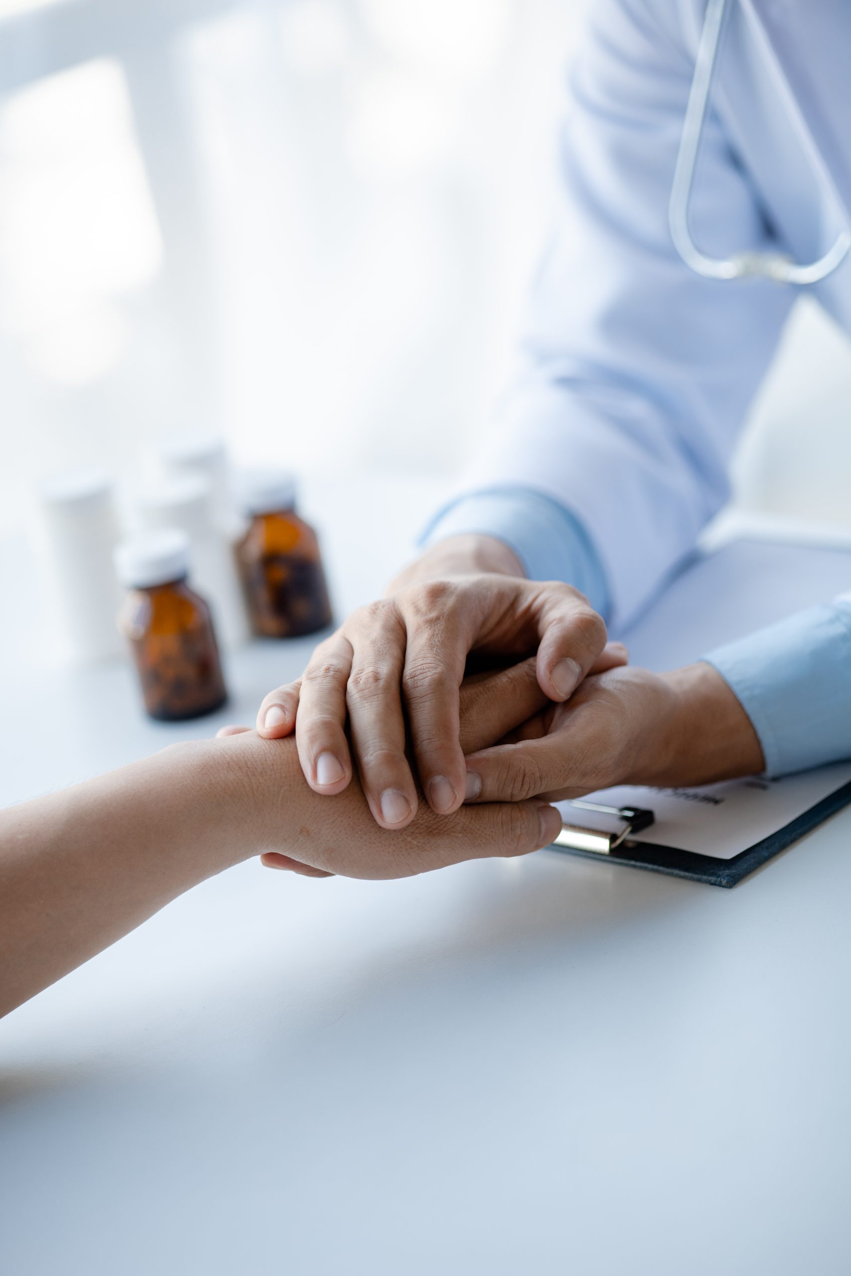 A GP near Malvern East offers a comforting hand to a patient; medicine bottles and clipboard are in the background.