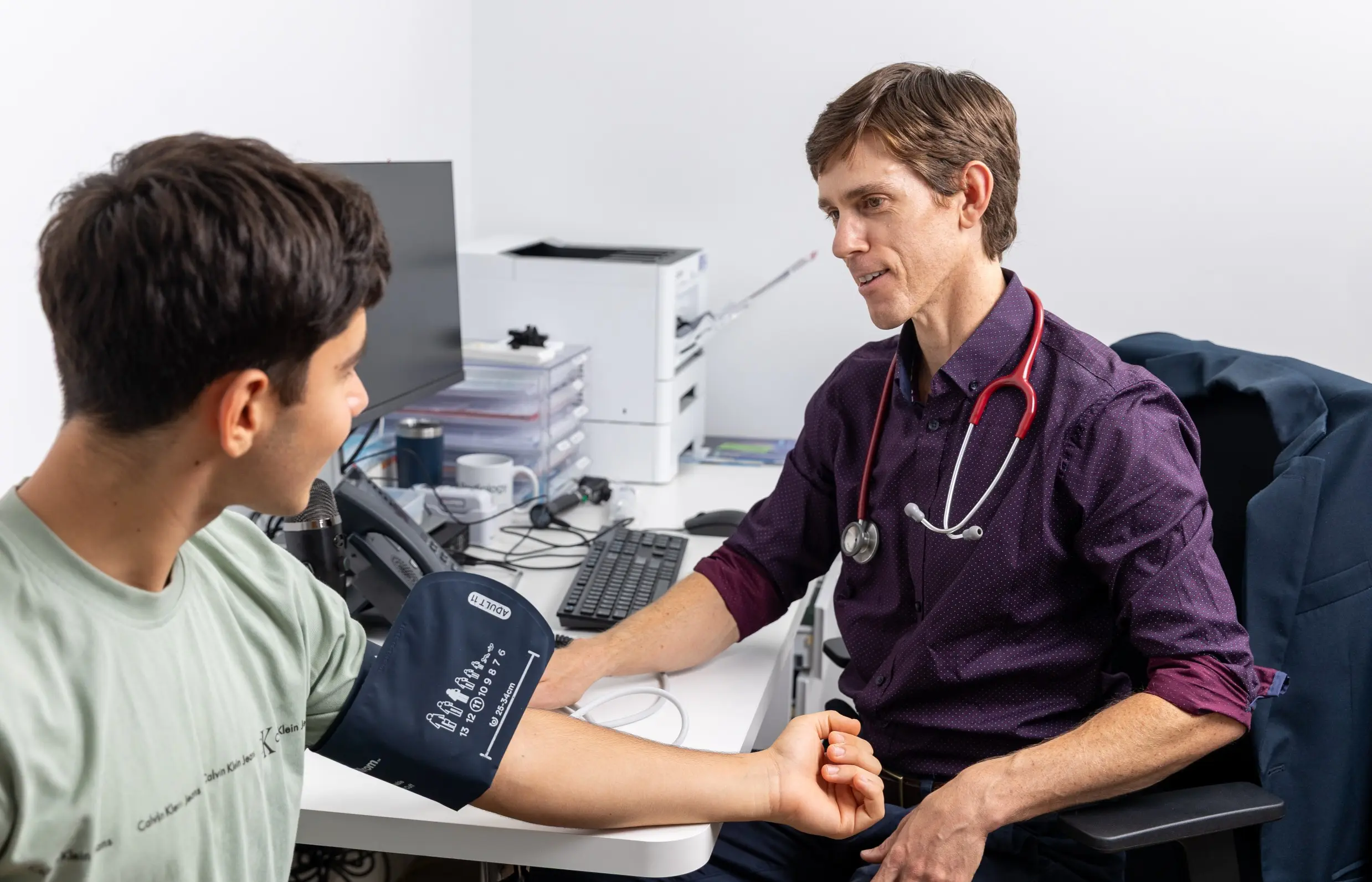 Dr Casey checks a patient’s blood pressure in a clinic, watching the monitor as the cuff is on his arm.