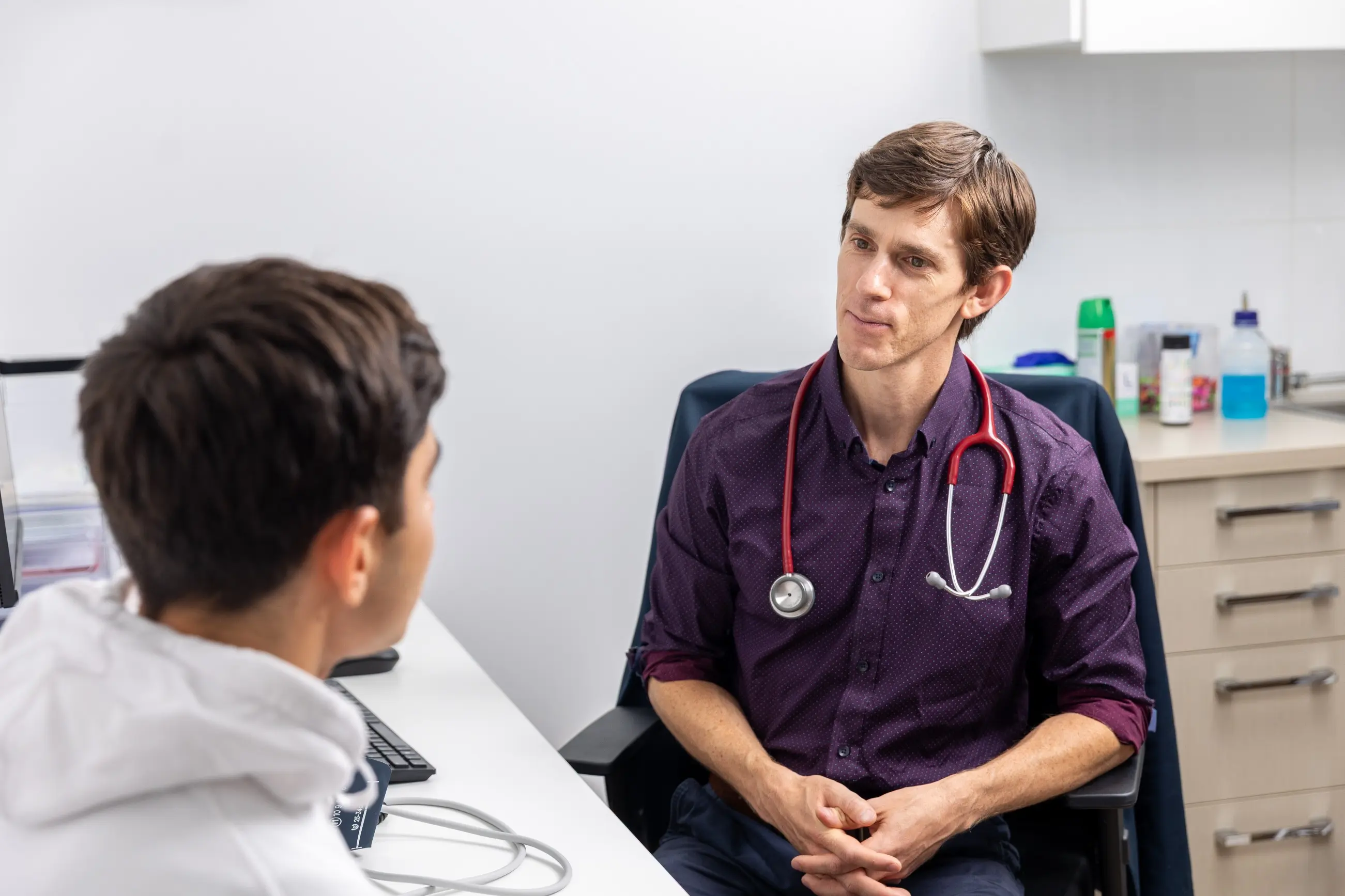 Dr Casey speaks with a patient about men’s health in the exam room, medical supplies visible in background.