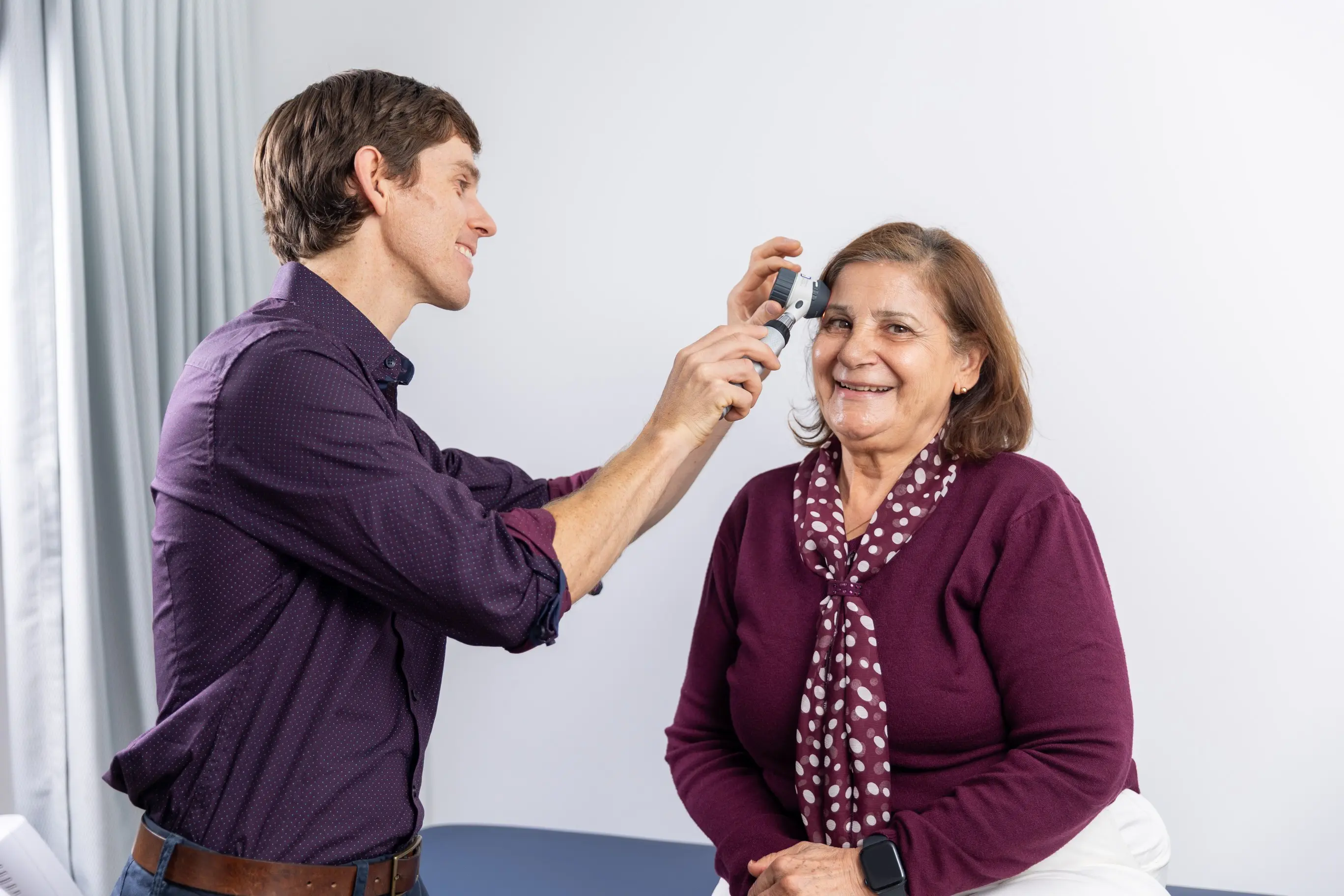 Dr Casey uses an otoscope to check a smiling woman’s ear during a Women’s Health visit.