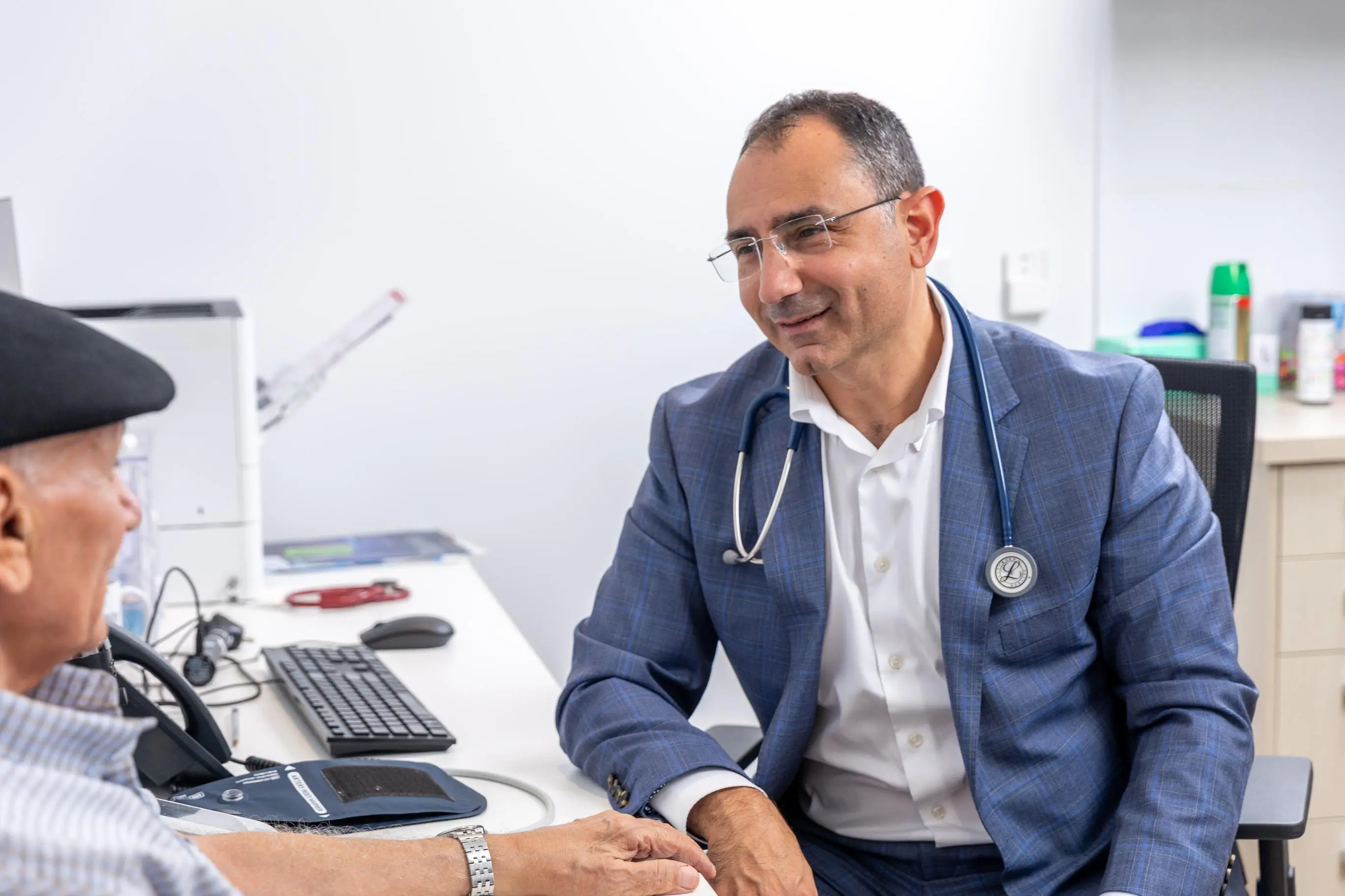 Dr Nadim, GP at Family Health Clinic, discusses health with an older male patient during a checkup in his office.