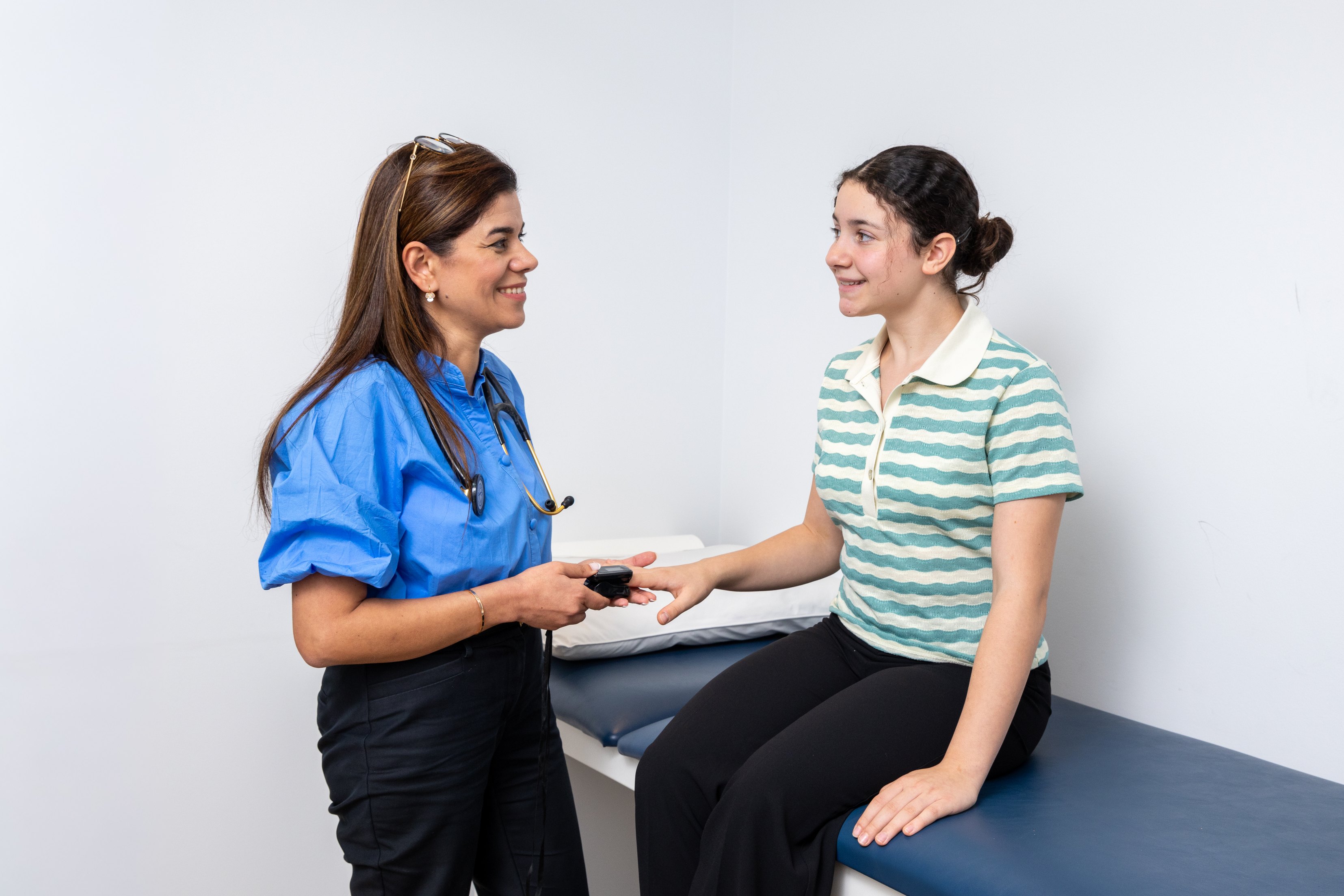 Dr Neda advises a young patient on travel health and vaccinations with a stethoscope in a medical office.