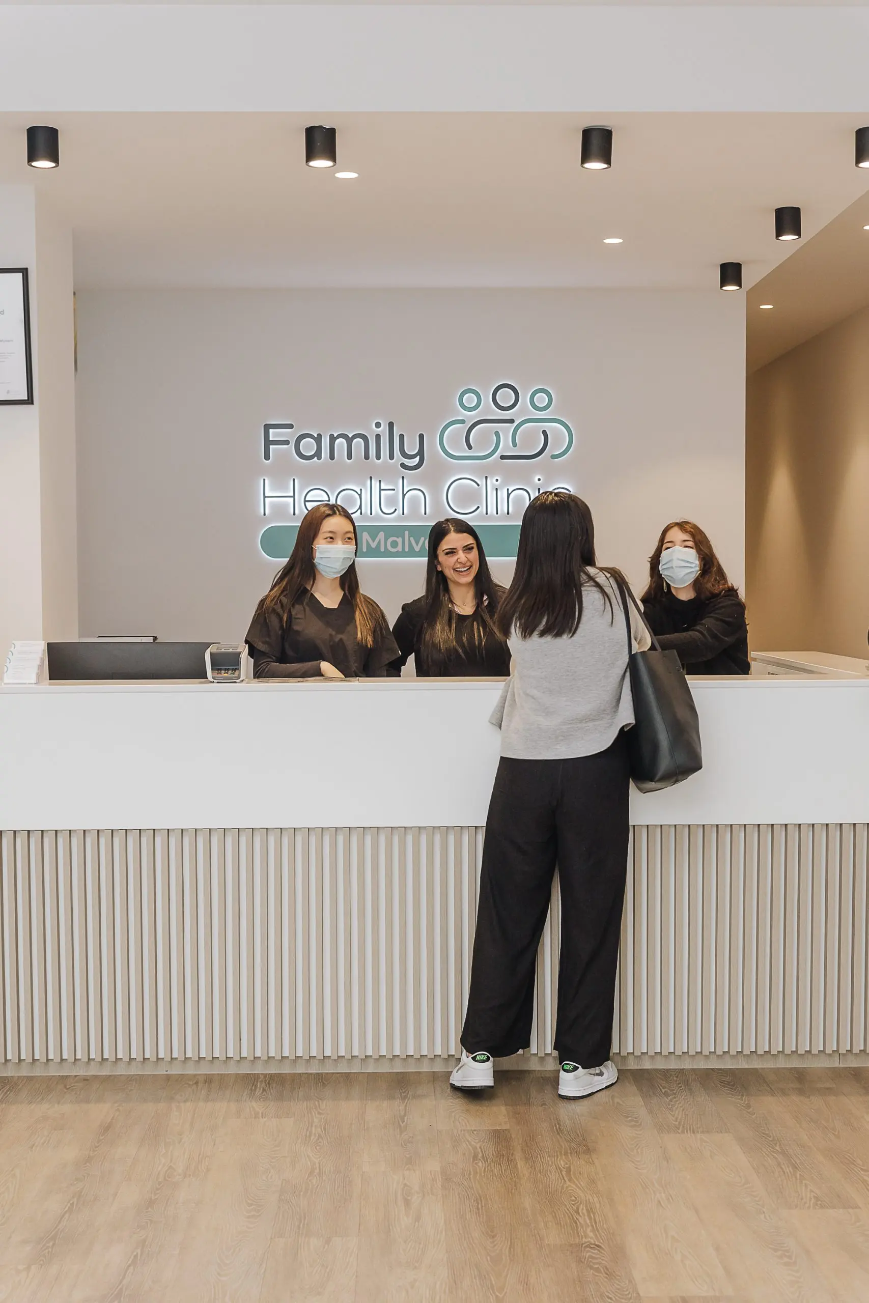 Woman at Family Health Clinic desk asks masked staff about continuity and follow-up Iron Infusion service.