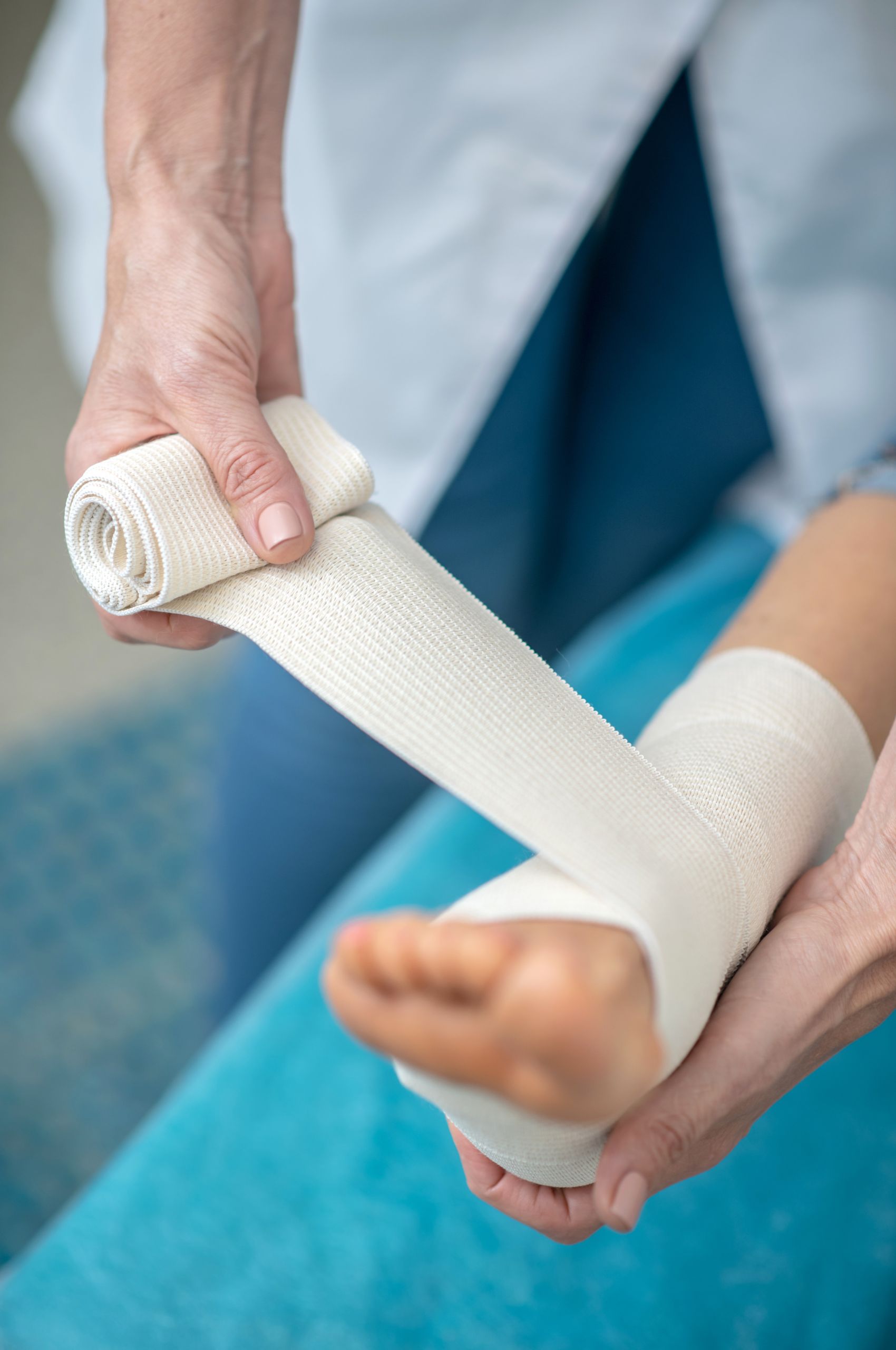 Medical professional wraps patient’s foot and ankle with white elastic bandage for Workcover or TAC treatment.